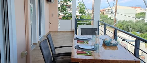 Un balcón con una mesa de madera lista para comer, sillas de mimbre y vistas del entorno.