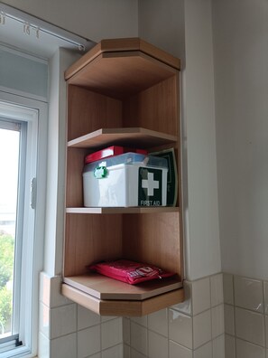 A corner cabinet with a first aid kit, a red box, and a white container with a green lid. - Perfect 1-bedroom apartment with AC in charming Kiato (Kiato)