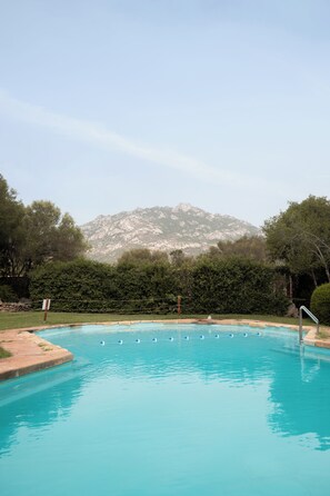 A swimming pool with clear blue water, surrounded by greenery and a mountain in the background. - Vera Holiday Home by Wonderful Italy (Olbia)
