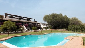 Una piscina amb solàrium enrajolat, envoltada d'un jardí ben cuidat i un edifici amb teulada inclinada.