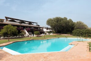 A swimming pool with a tiled deck, surrounded by a landscaped garden and a building with a sloped roof. - Vera Holiday Home by Wonderful Italy (Olbia)