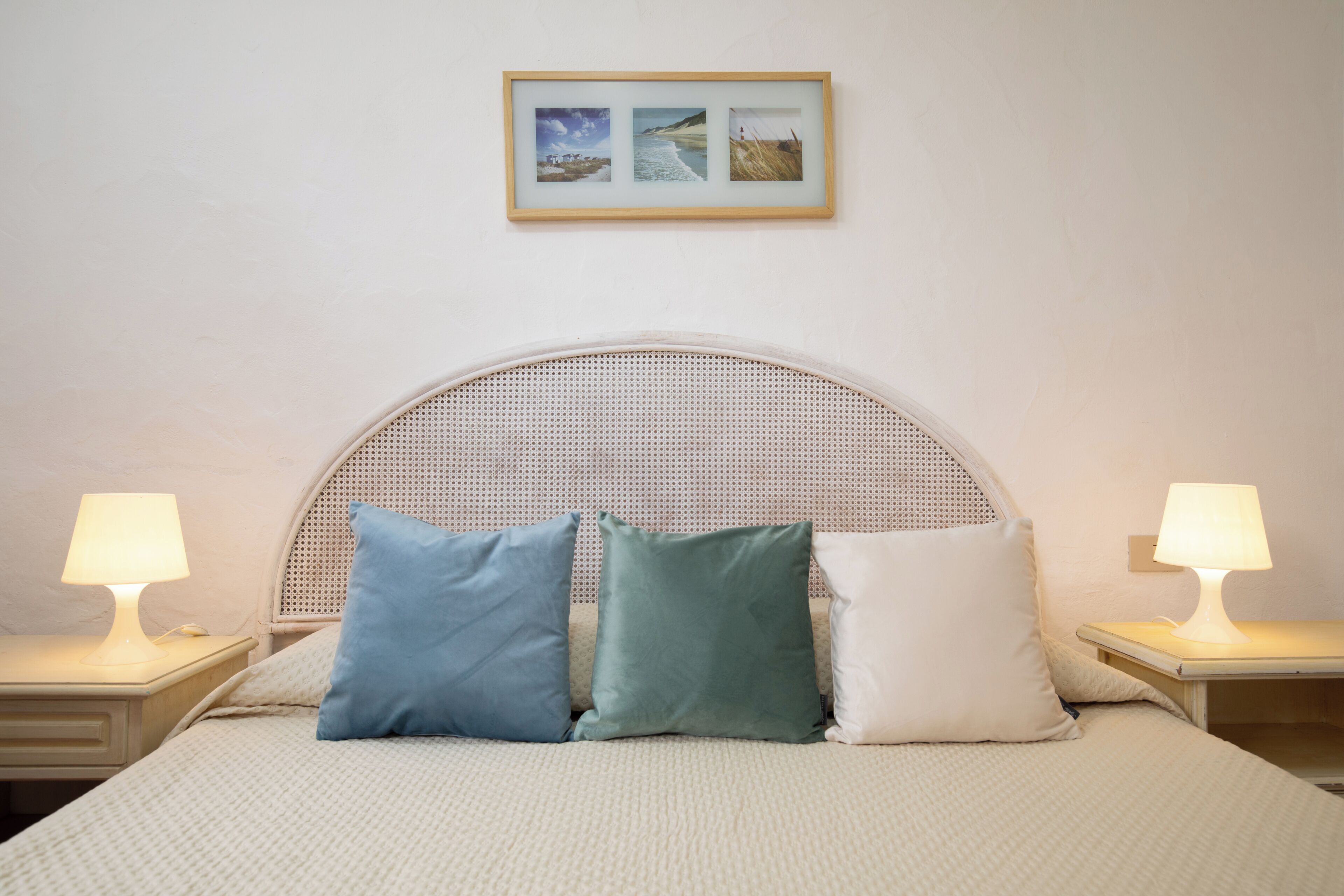 A bed with a woven headboard, two bedside lamps, and three pillows.