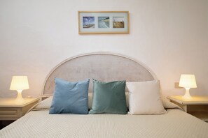 A bed with a woven headboard, two bedside lamps, and three pillows. - Vera Holiday Home by Wonderful Italy (Olbia)
