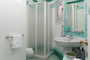 A bathroom with a white toilet, a glass-enclosed shower, a sink with a mirror above it, and toiletries on the counter. - Vera Holiday Home by Wonderful Italy (Olbia)
