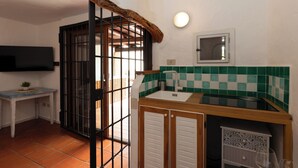 Cuina amb rentatge, fogó i finestra. Hi ha un televisor fixat a la paret i una porta amb reixatge metàl·lic.