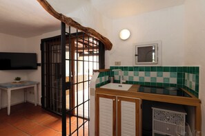 A kitchen with a sink, a stove, and a window. There is a television mounted on the wall and a door with a metal gate. - Vera Holiday Home by Wonderful Italy (Olbia)