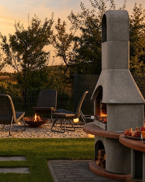 Eine Terrasse im Freien mit Grill aus Stein, zwei Korbstühlen und einer Feuerstelle.