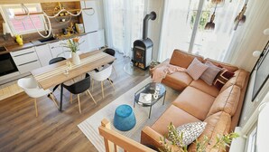 A modern living space with a wooden floor, a sofa, a dining table with chairs, a kitchen area, and a wood-burning stove. - Design retreat with sauna near Berlin (Wandlitz)