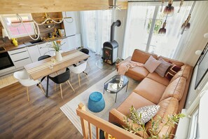 Ein zeitgemäßer Wohnraum mit Holzboden, einer Couch, einem Esstisch mit Stühlen, einer Küchenzeile und einem Kaminofen.