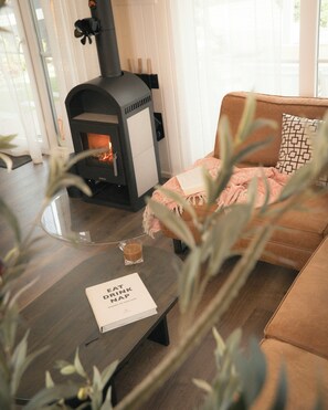 A cozy living room with a modern fireplace, a comfortable sofa, a glass coffee table, and a book titled 'EAT DRINK NAP'.