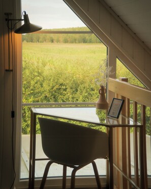 Una habitación con vistas a un campo verde, una silla, un escritorio y una lámpara.