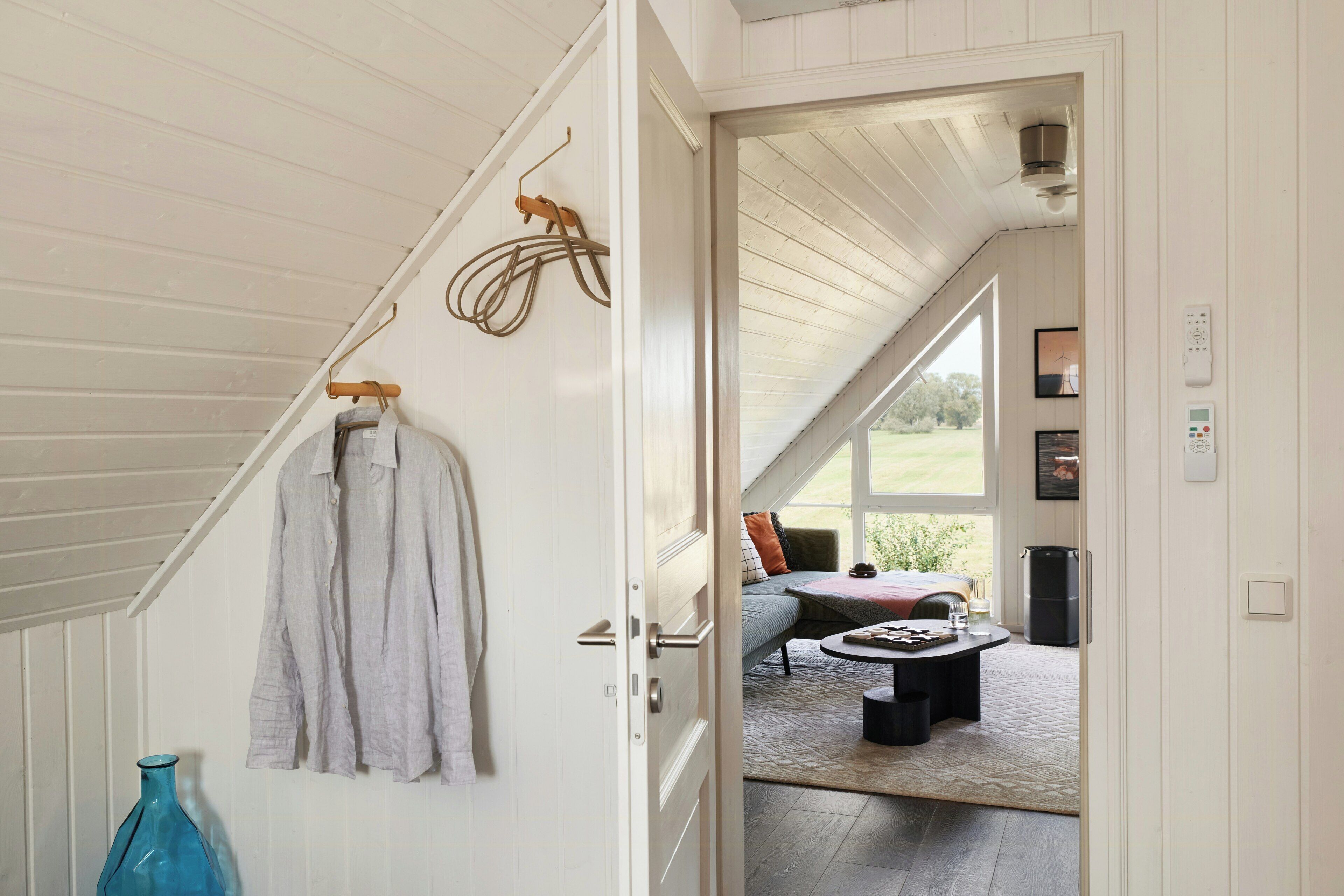 A room with a high ceiling, a hanging coat rack, a bed with a view, and a small table with items on it.