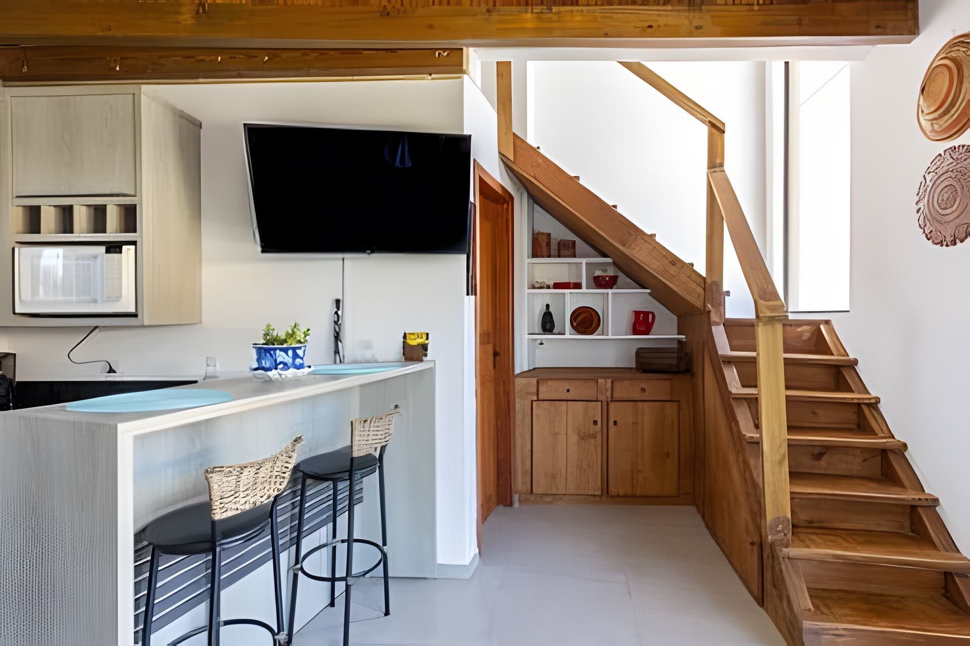 A modern kitchen with a built-in TV, wooden bar stools, and a staircase leading to a loft area.