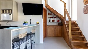 Una cocina moderna con televisor integrado, taburetes de madera y una escalera que conduce a una zona de altillo.
