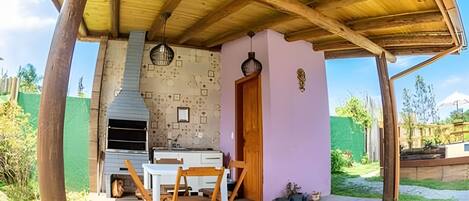 An outdoor patio with a wooden table and chairs, a built-in grill, and a door leading to a garden.