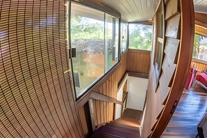 A wooden staircase leading to a balcony with a view of a backyard.