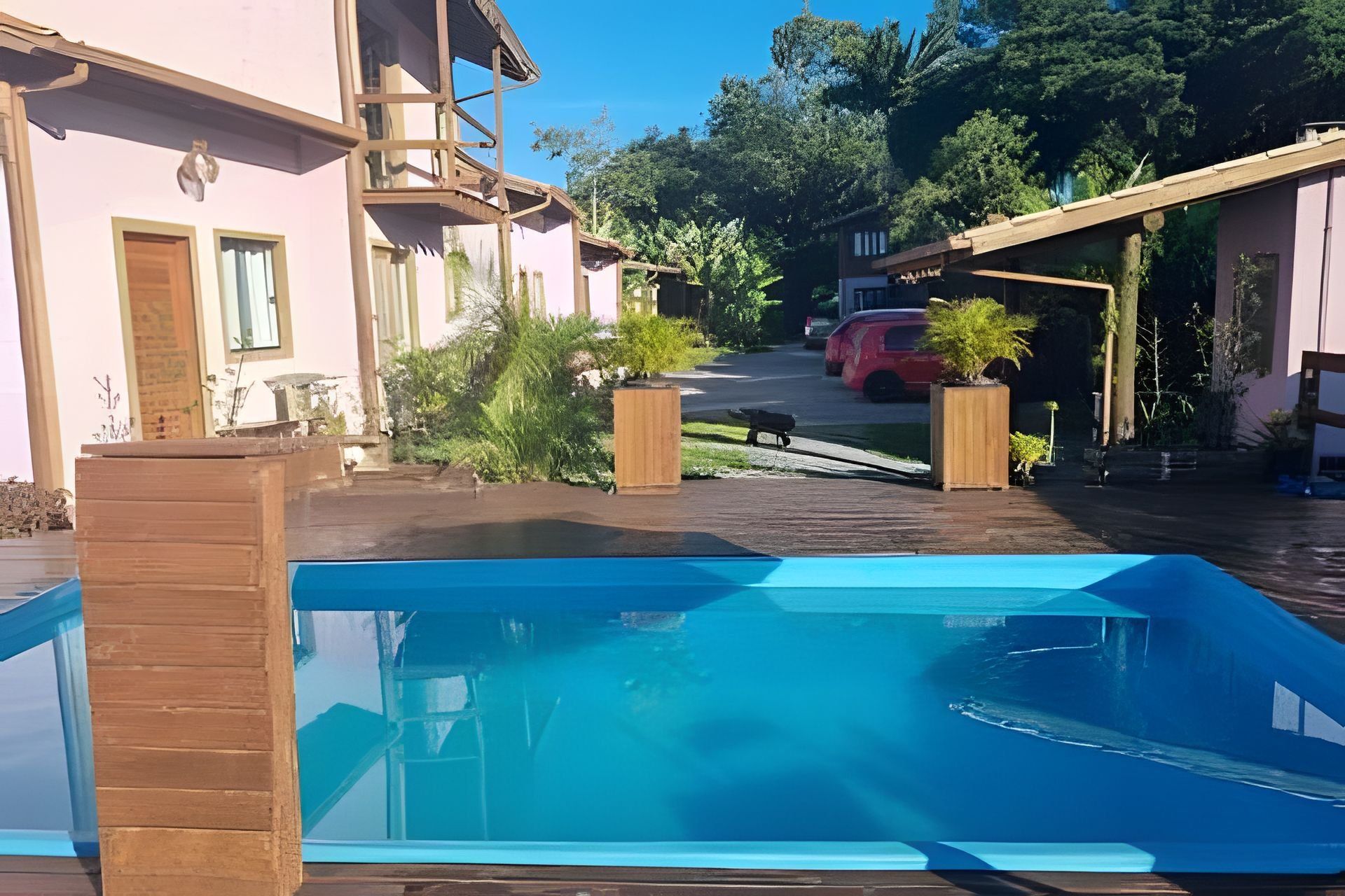 Um bairro residencial com piscina, deck de madeira e um carro vermelho estacionado ao fundo.
