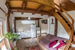A cozy interior with a wooden ceiling, a kitchen area with a refrigerator and microwave, and a sofa with cushions.