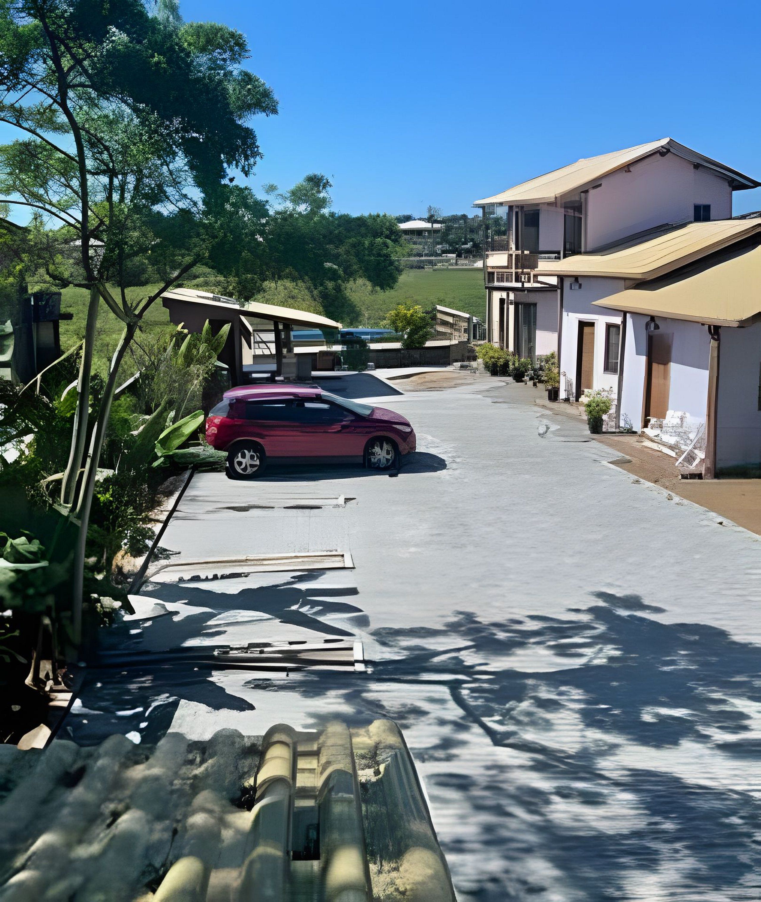 Zona residencial con entrada pavimentada, un coche estacionado y casas con balcones.