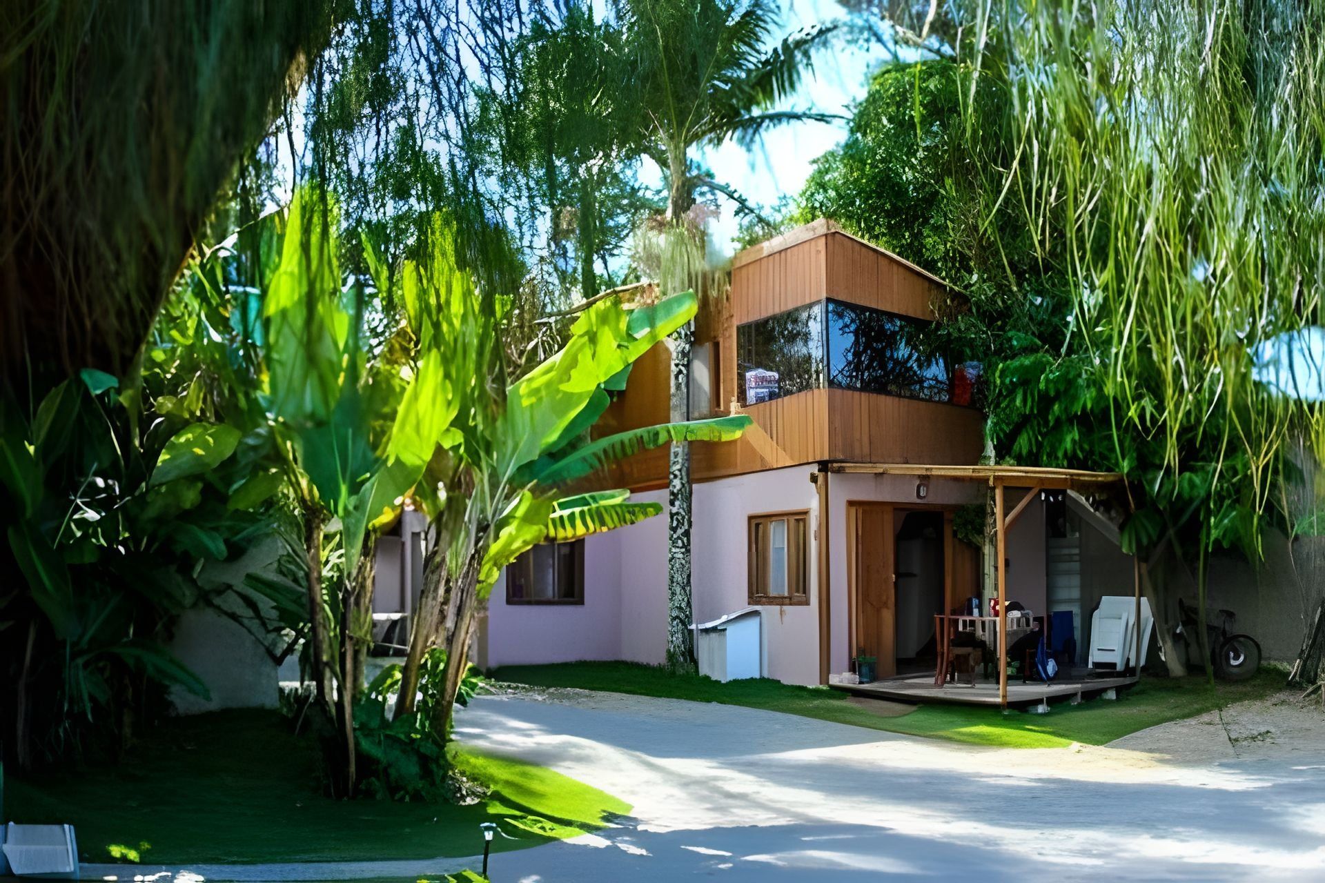 A two-story house with a balcony, surrounded by lush greenery.