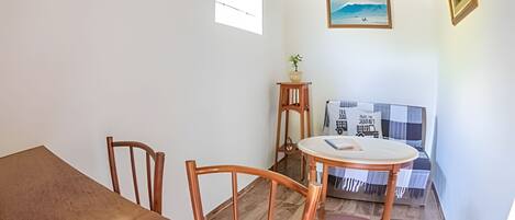A dining area with a wooden table and chairs, a small round table with a single chair, a potted plant, and a framed picture on the wall.
