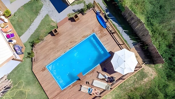 A rectangular swimming pool with a wooden deck, surrounded by a grassy area and a wooden fence.