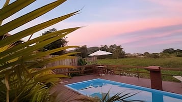 A swimming pool with a wooden deck, surrounded by a fence and palm trees.