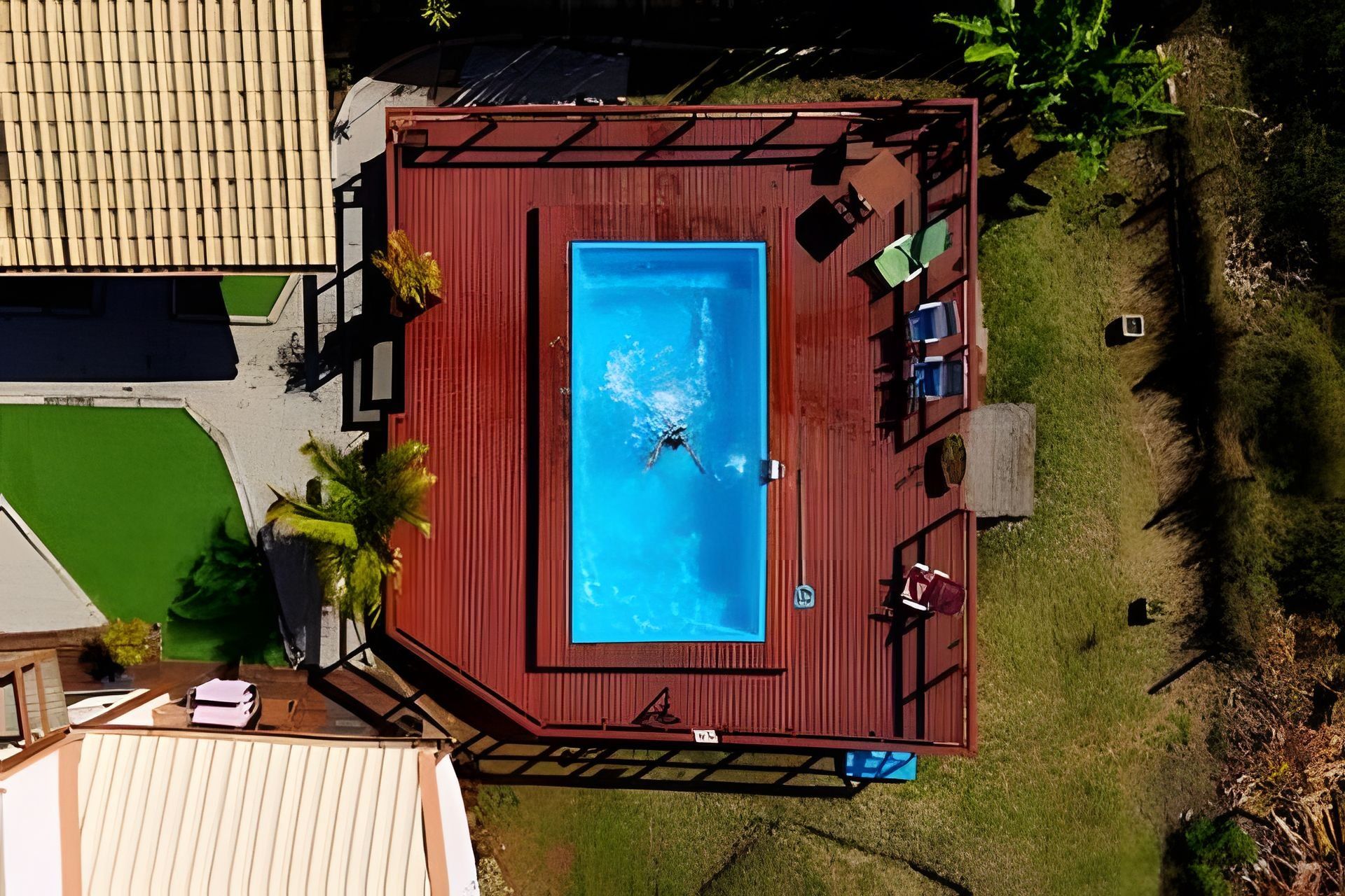 An aerial view of a swimming pool with a deck, surrounded by grass and a few trees.