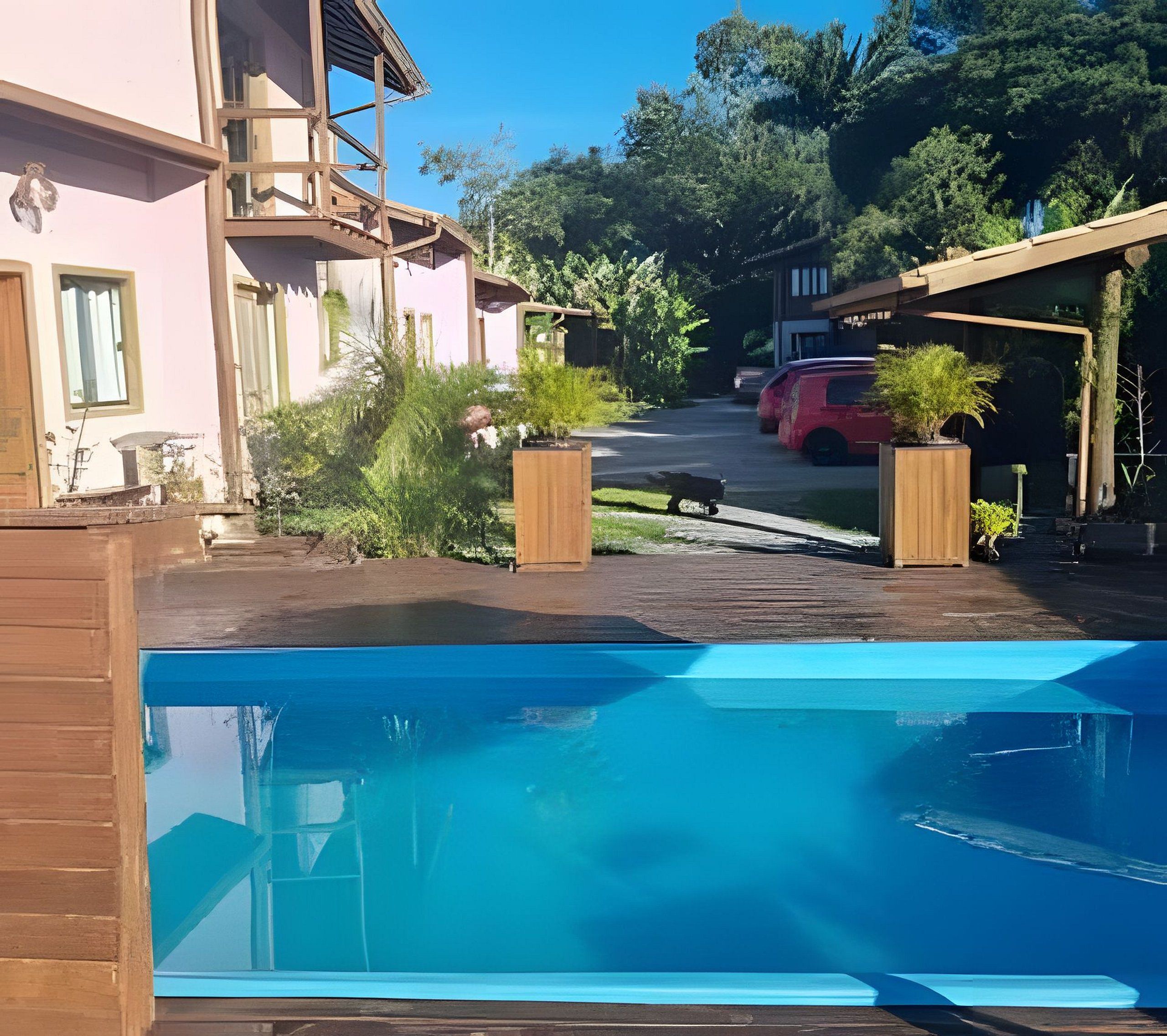 Una propiedad residencial con piscina, un vehículo rojo estacionado en la entrada y un jardín con plantas en macetas.