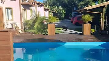 Una propiedad residencial con piscina, un vehículo rojo estacionado en la entrada y un jardín con plantas en macetas.
