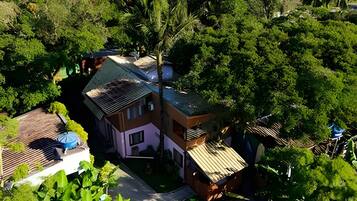 A two-story house with a sloped roof, surrounded by dense greenery.