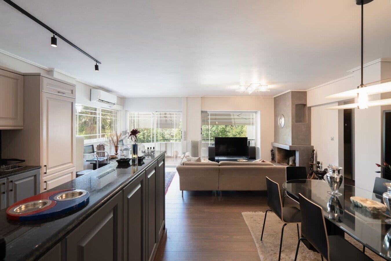 A modern kitchen with a central island, a dining area with a glass table, and a living room with a sofa and TV.