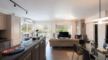 A modern kitchen with a central island, a dining area with a glass table, and a living room with a sofa and TV.