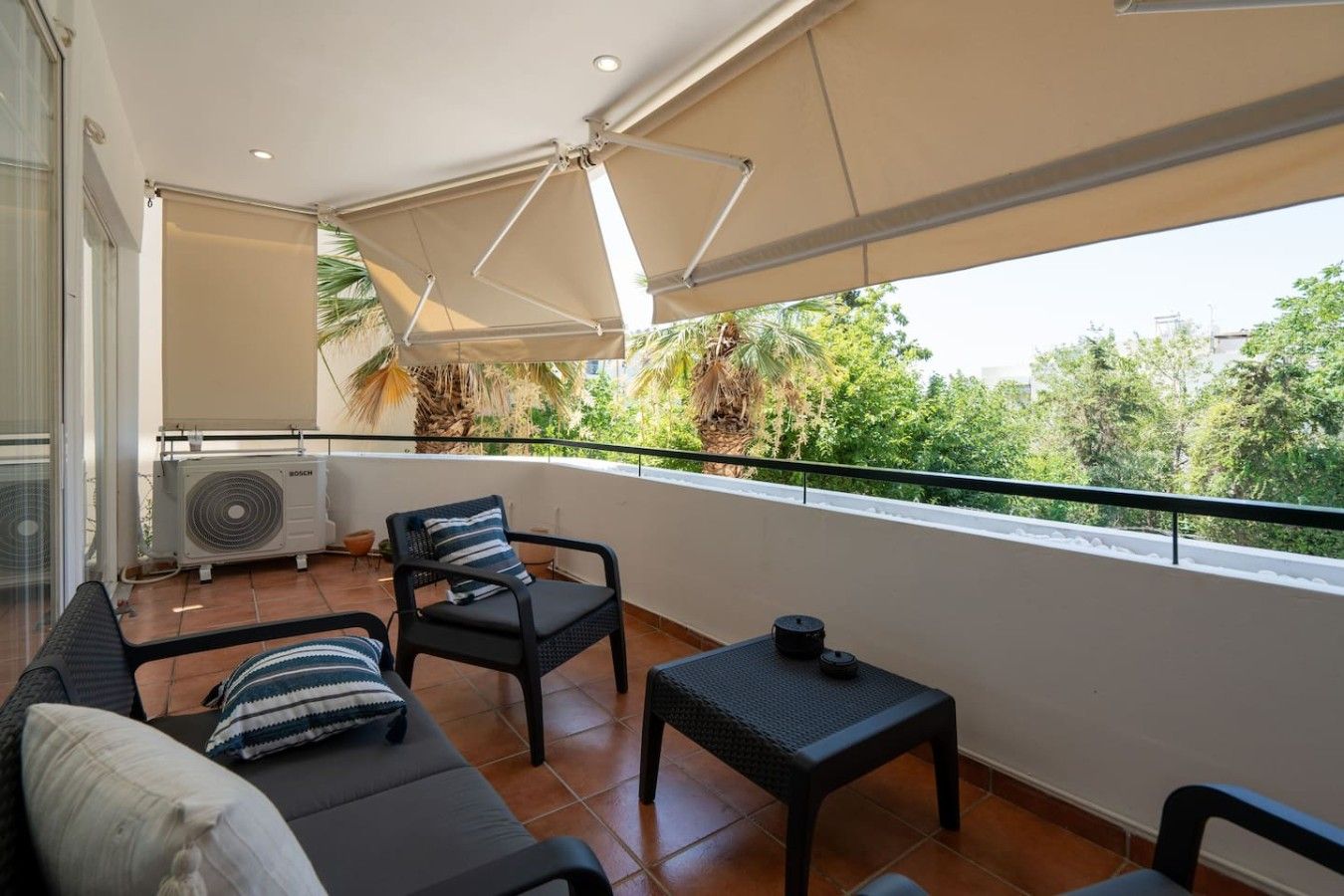 A balcony with a sofa, two chairs, a small table, and a ceiling fan.