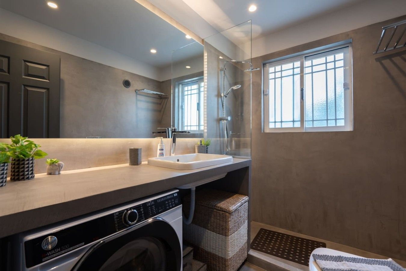 A modern bathroom with a built-in washing machine, a large mirror, and a shower enclosure.