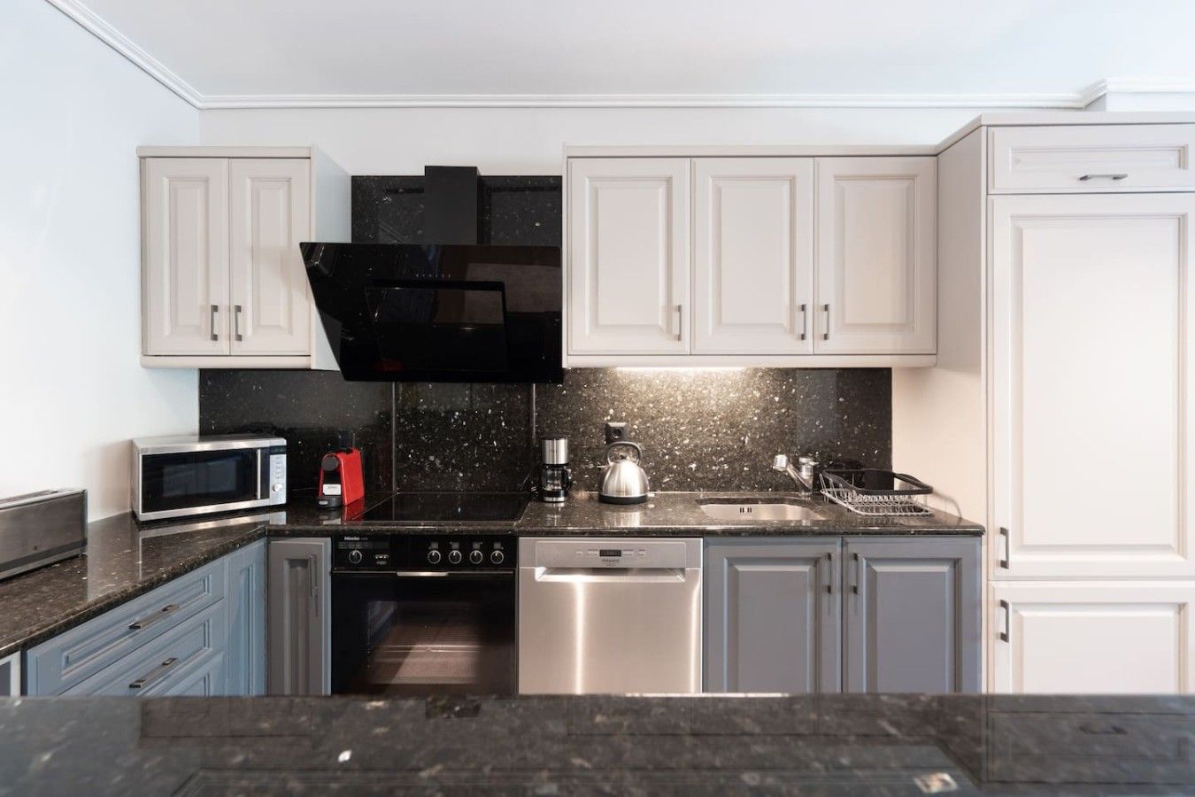 A modern kitchen with white cabinets, a black range hood, stainless steel appliances, and a granite countertop.