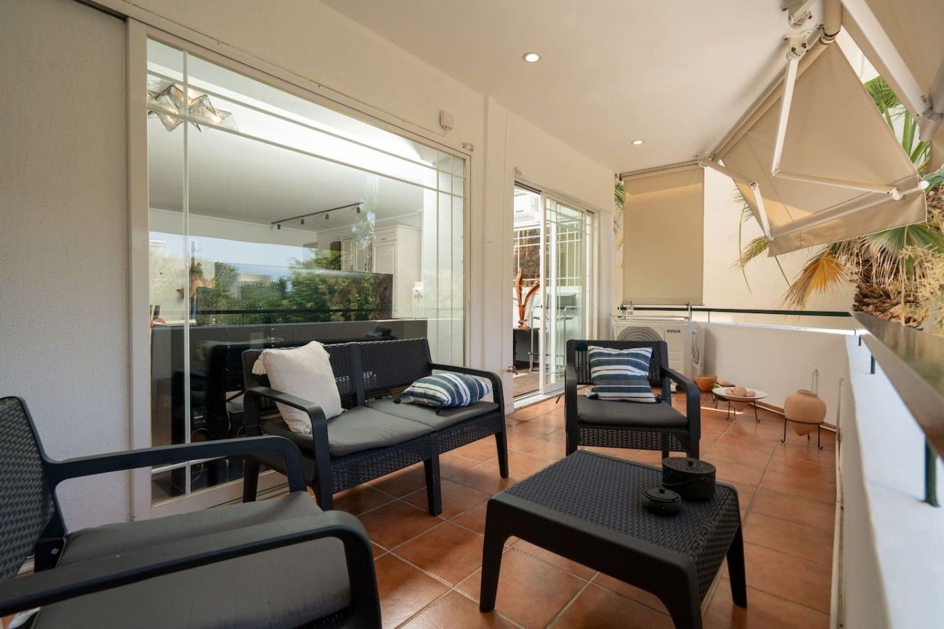 A balcony with a sofa, chairs, and a table, featuring a glass door leading to a patio area.