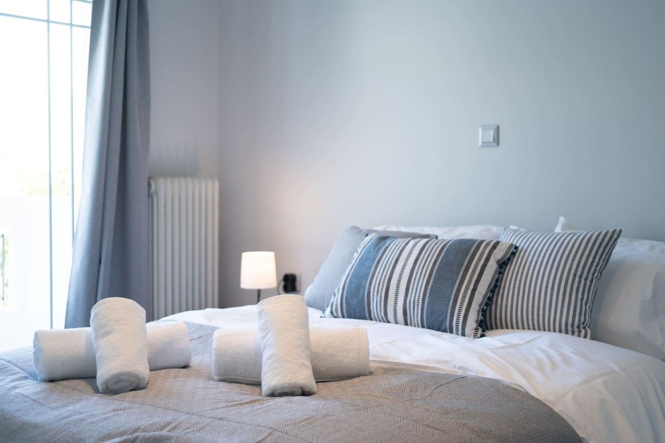 A hotel room with a bed, pillows, a lamp, and a radiator.