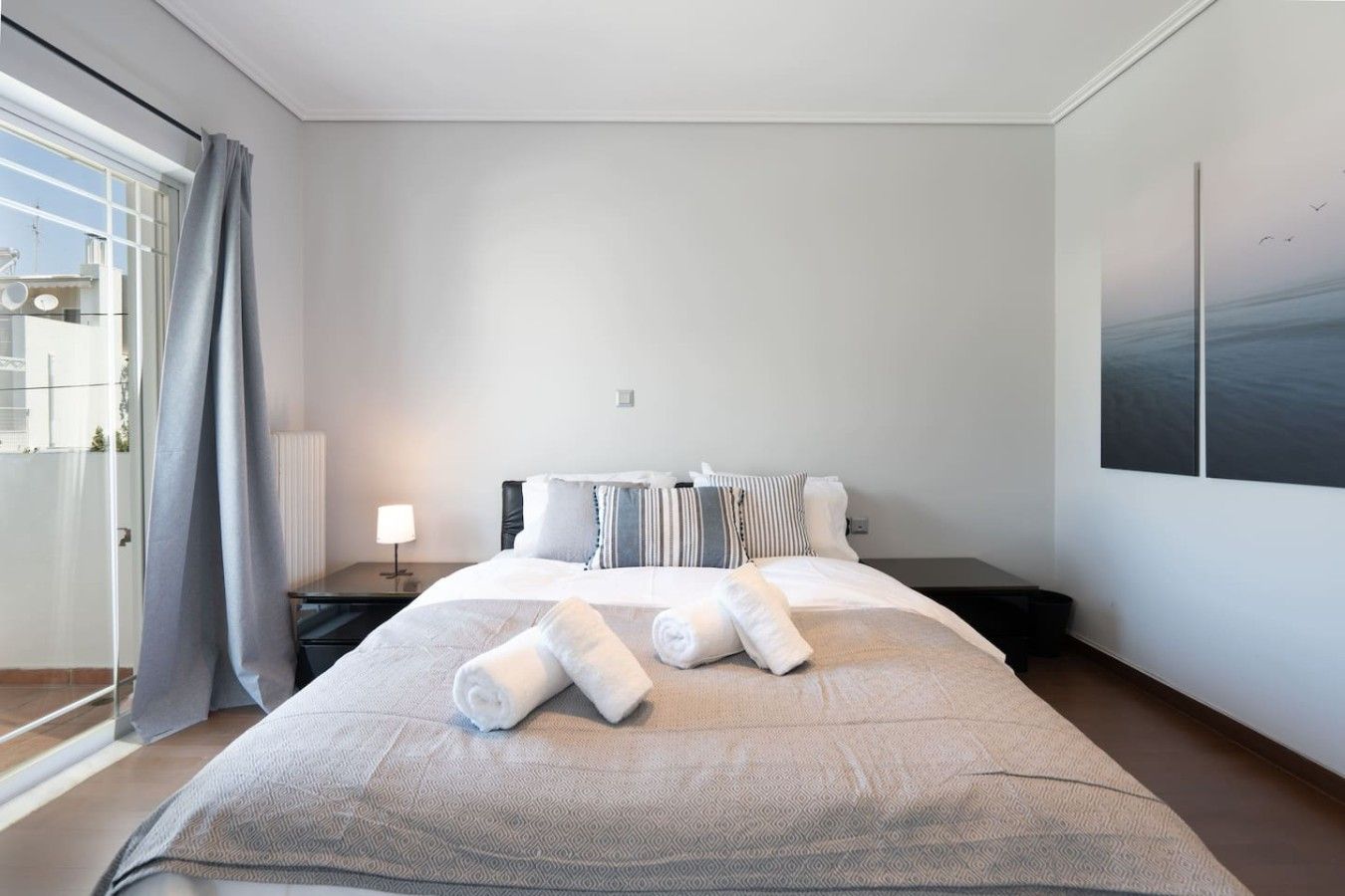A hotel room with a large bed, a nightstand, a lamp, and a view of the sea through the window.