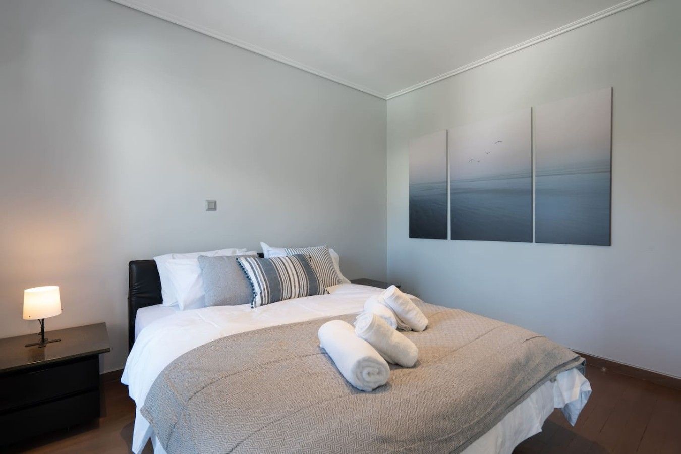 A modern bedroom with a large bed, a nightstand, a lamp, and a wall-mounted artwork.