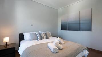A modern bedroom with a large bed, a nightstand, a lamp, and a wall-mounted artwork.