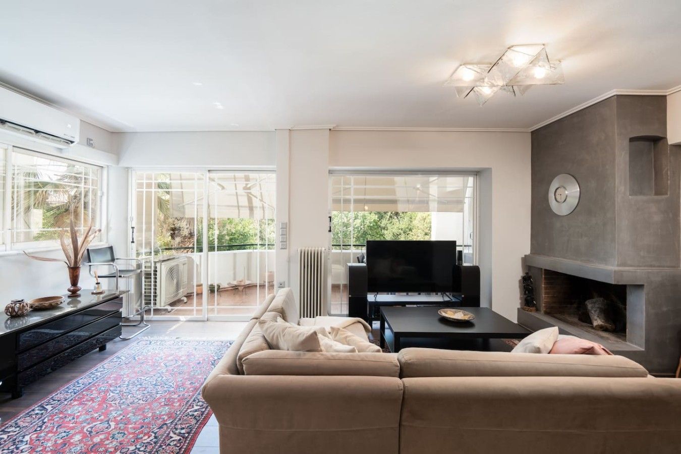 A modern living room with a sofa, TV, fireplace, and large windows.