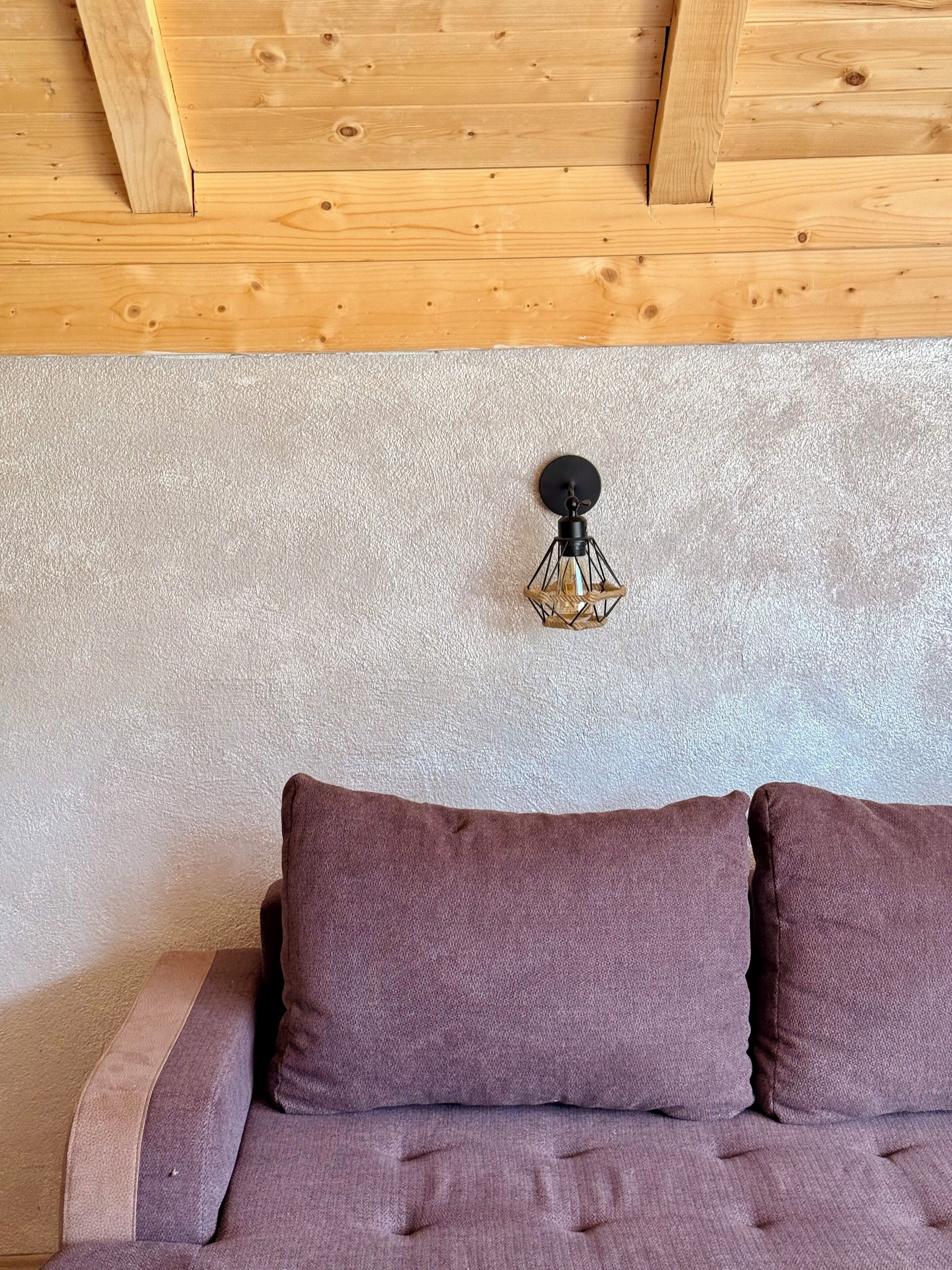 A room with a wooden ceiling, a textured wall, and a bed with two pillows.