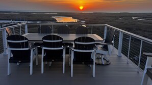 A deck with a table and chairs overlooking a sunset over a water body. - Tranquil 1-bedroom house with AC on charming Smith Island (Smith Island)
