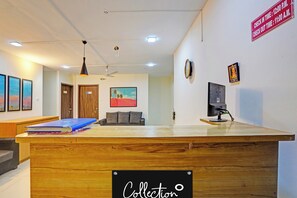 A reception desk with a sign indicating check-in and check-out times, a ceiling fan, a painting on the wall, and a television on a stand. - Super Collection O Baner Hillview Pune (Pune)