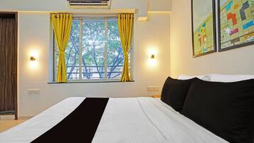 A hotel room with a bed, a window with curtains, an air conditioner, and wall-mounted lights.