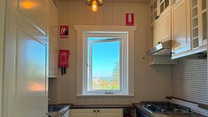 Cocina compacta con ventana, armarios blancos, estufa a gas y extintor.