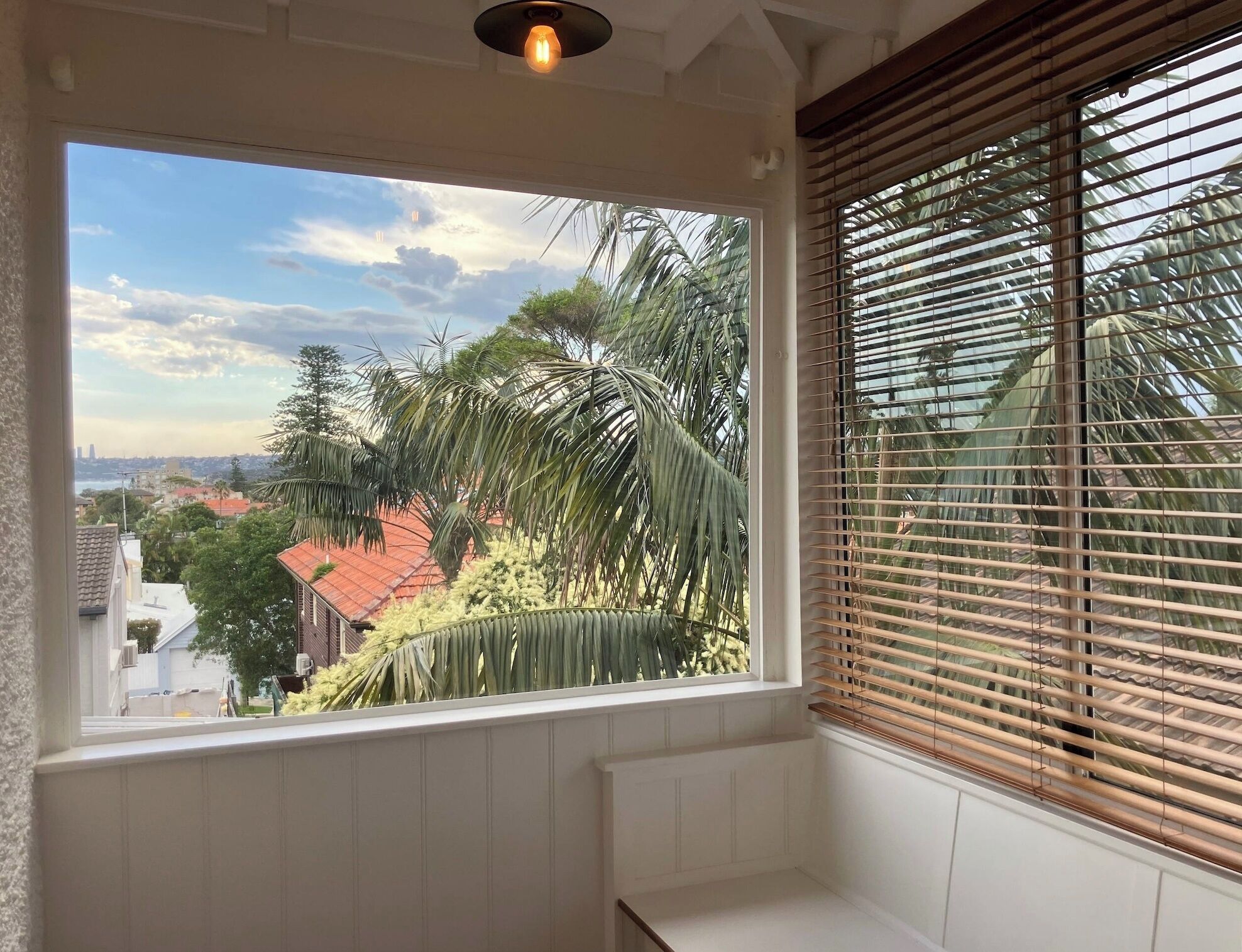 Ein Zimmer mit großem Fenster, Blick auf eine Wohngegend mit Palmen und einem Gebäude mit rotem Dach.