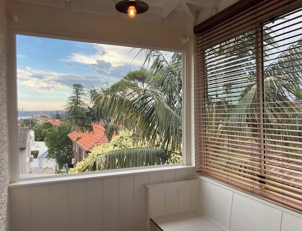 A room with a large window overlooking a residential area with palm trees and a red-roofed building.