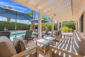 An outdoor patio with a pool, lounge chairs, umbrellas, and a pergola structure. - *Home - 570 N Lujo Cir, Palm Springs (Palm Springs)